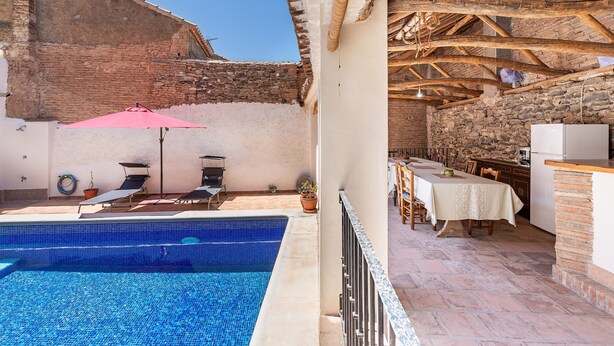 A poolside area with a pool, lounge chairs, a table, and a kitchen area.