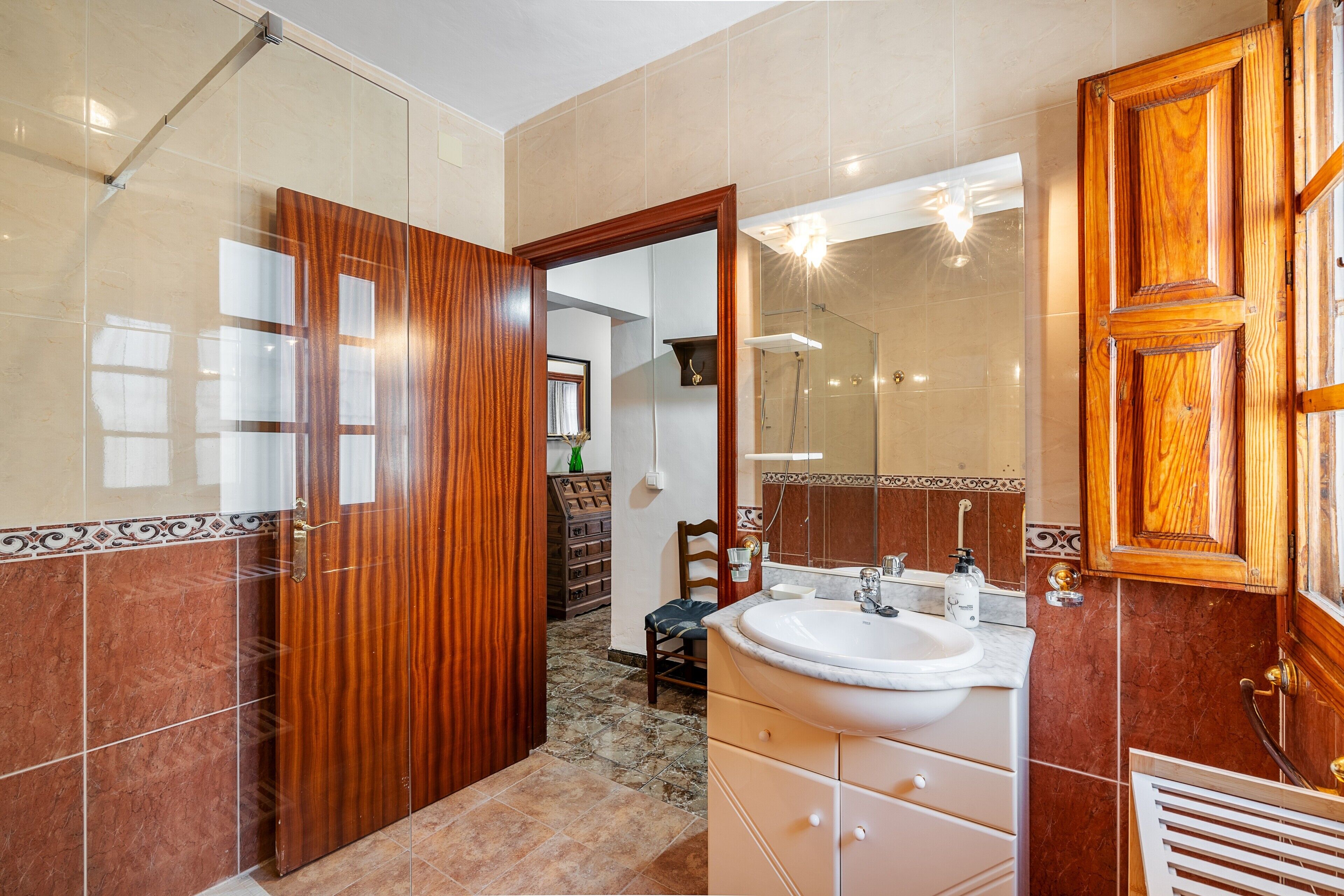 A bathroom with a glass shower enclosure, a wooden door, a white sink, and a mirror.