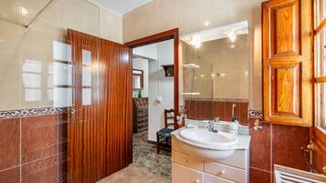 A bathroom with a glass shower enclosure, a wooden door, a white sink, and a mirror.