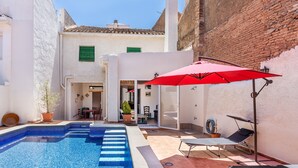 A swimming pool with steps, a red umbrella, and two sun loungers.