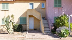 A two-story building with a staircase leading to the entrance, a small garden area with plants, and a door with a window above it.