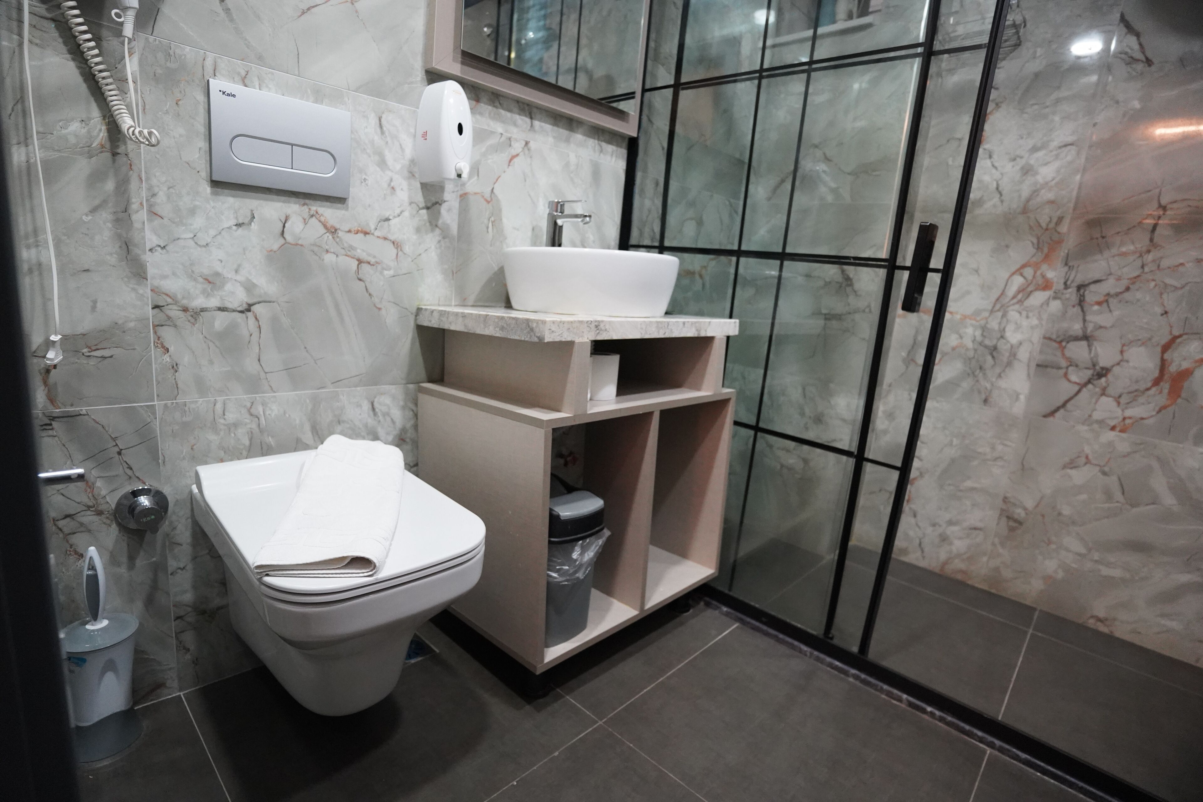 A modern bathroom with a toilet, a sink, a shower, and a marble-tiled wall.