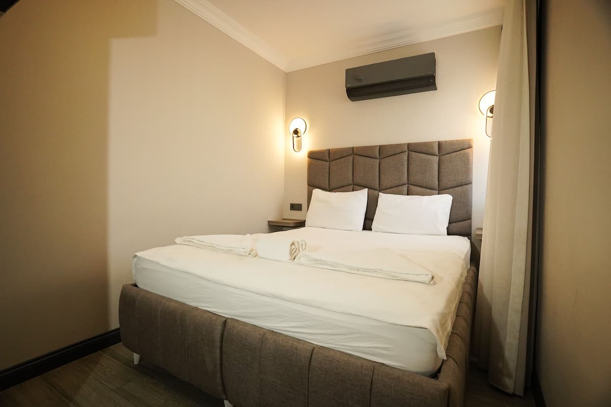 A hotel room with a large bed, a headboard, two bedside tables, and a wall-mounted air conditioner.