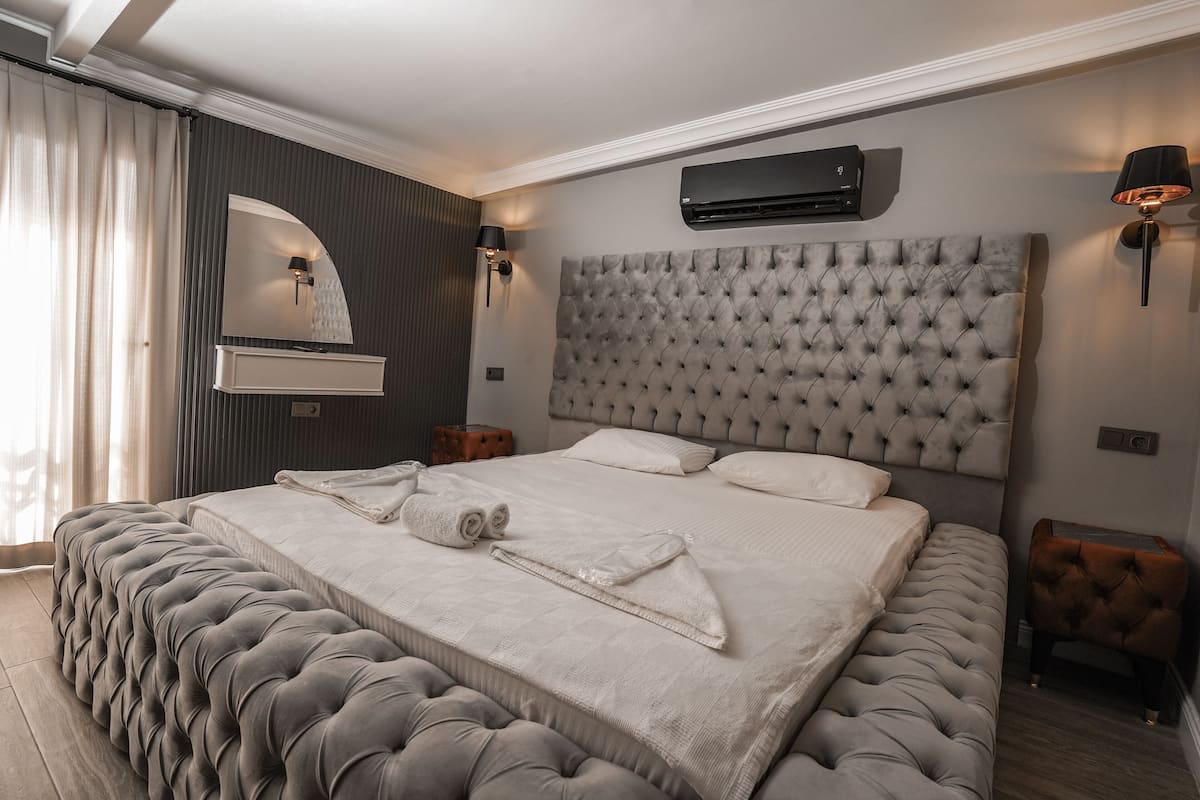 A large bed with a tufted headboard, a wall-mounted air conditioner, and a bedside lamp.