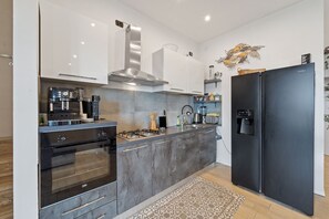 A modern kitchen with a built-in oven, a stove, a black refrigerator, and a stainless steel range hood.