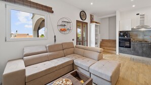 A modern living room with a sectional sofa, a wooden coffee table, and a kitchen area with dark cabinets and a stainless steel range hood. - Holiday Home "Villa Matteo Suite" with Sea View, Shared Pool and Wi-Fi (Perd'e Sali CA)