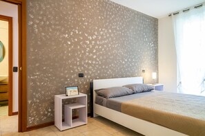 A bedroom with a bed, nightstands, a small shelf, and a wall with a floral pattern.