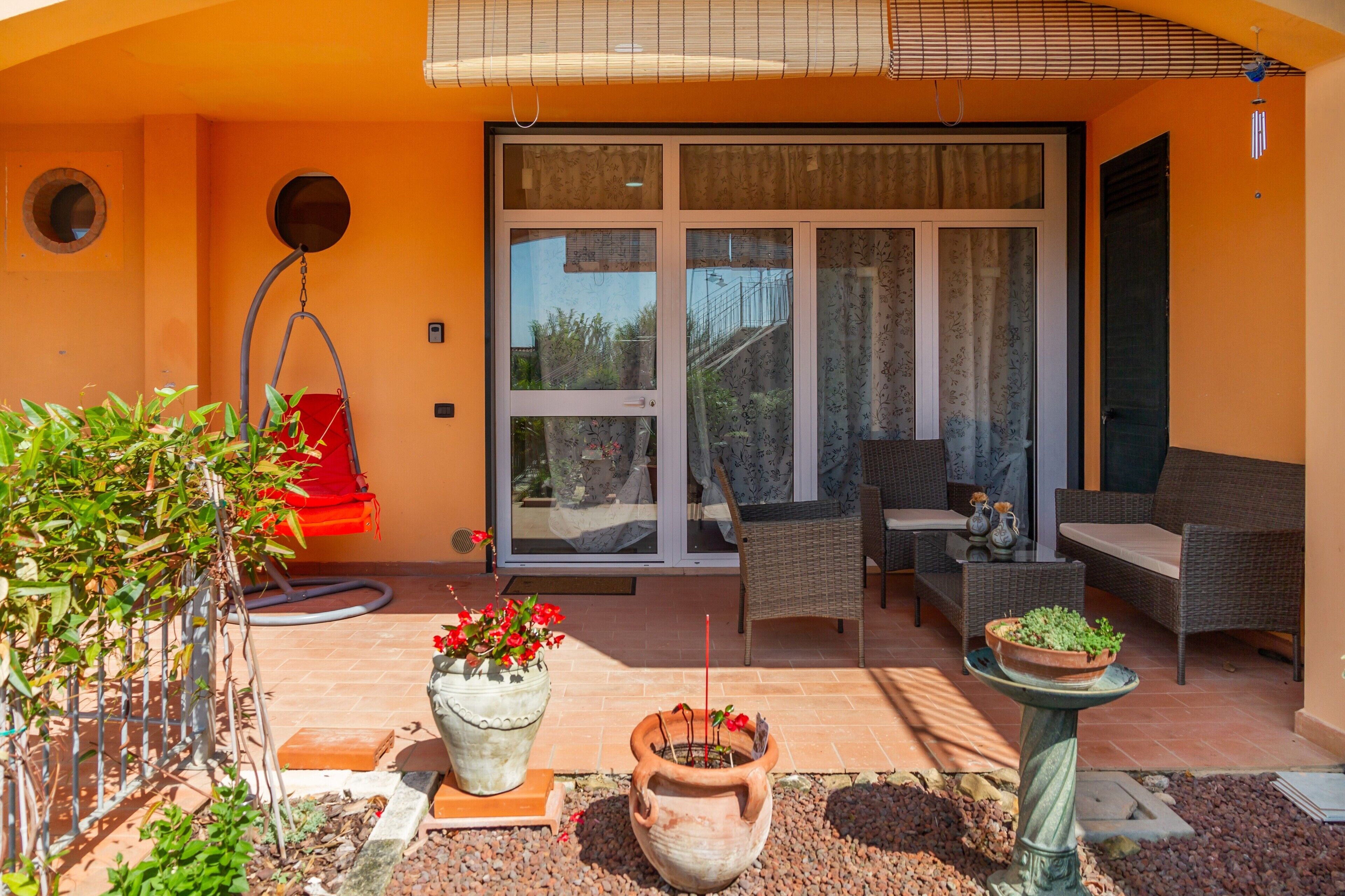 Une terrasse dotée de mobilier d’extérieur, de plantes en pot et d’une porte-fenêtre coulissante donnant sur un espace intérieur.
