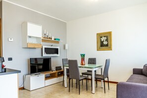 A modern living room with a flat-screen TV, a dining table with chairs, a sofa, and a framed artwork on the wall.
