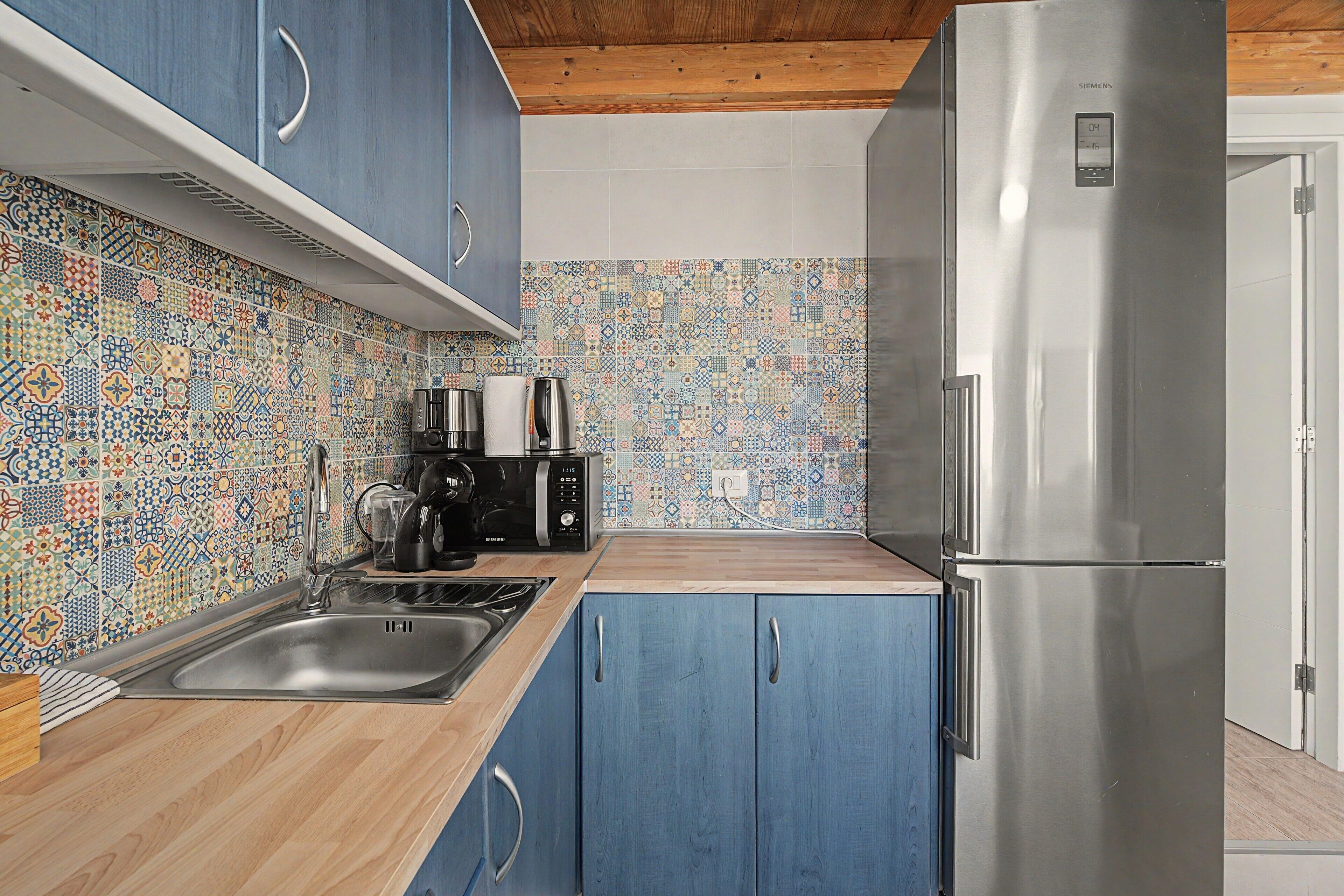 Een keuken met blauwe kastjes, een roestvrijstalen koelkast, een magnetron en een koffiezetapparaat.