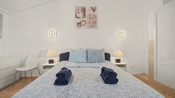 Ein modernes Schlafzimmer mit einem Bett, zwei Nachttischlampen, einem Sessel und einem Wandbild.