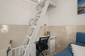 A bedroom with a white desk, a black office chair, a blue sofa, and a white ladder.