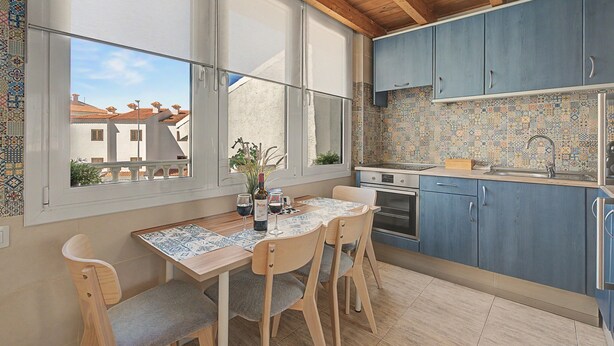 A kitchen with a dining area, featuring a table with chairs, a window with blinds, and a view of buildings outside. - Vacation Home "Torviscas Alta Vista" with Mountain View, Shared Pool & Wi-Fi (Costa Adeje)