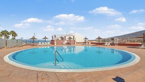 Ein Pool auf dem Dach mit klarem, blauem Wasser, umgeben von Liegestühlen und Sonnenschirmen, mit Blick auf die Skyline der Stadt.