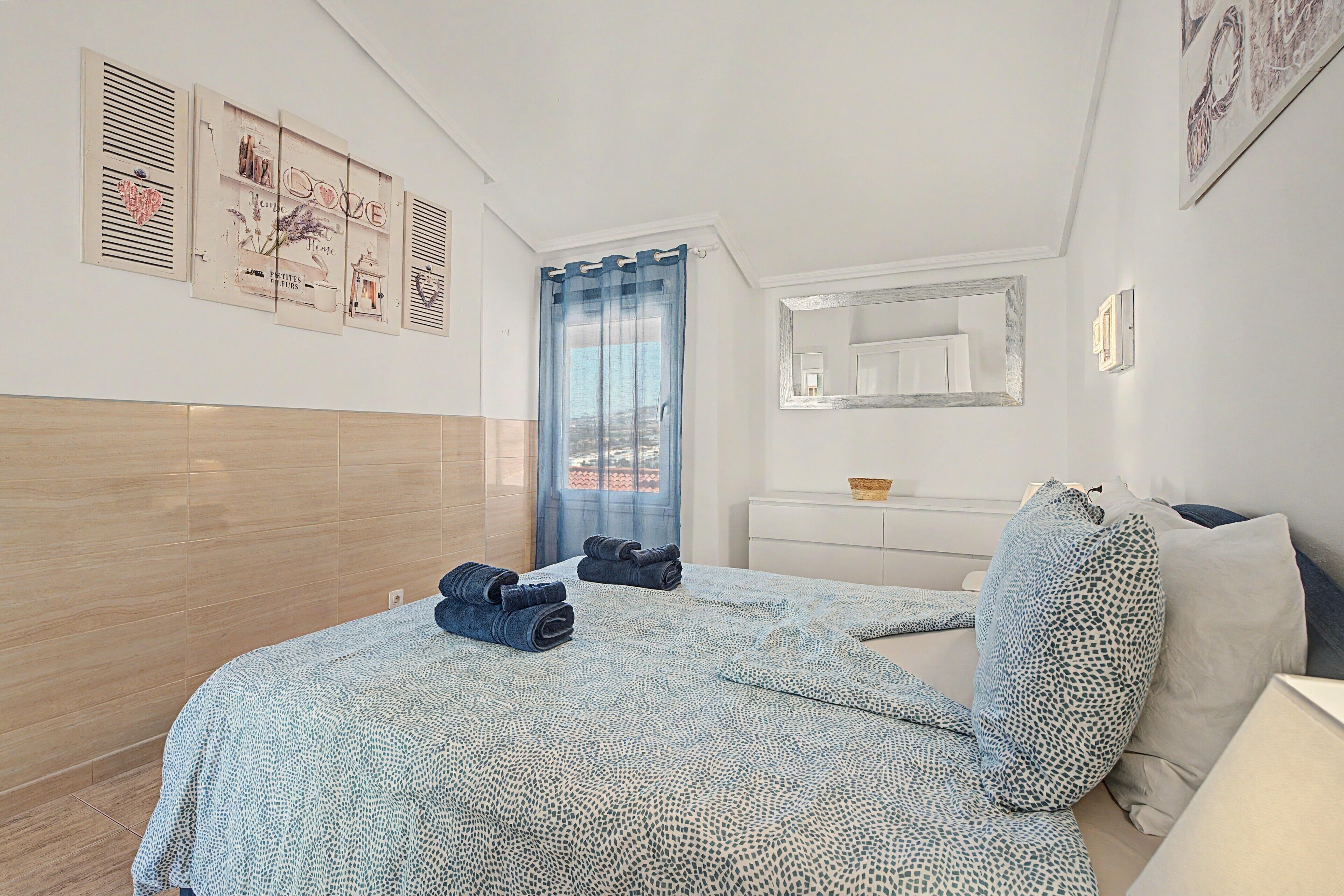 Une chambre à coucher avec un lit, une commode, un miroir et des œuvres d’art accrochées au mur.