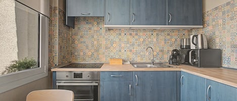 Cocina compacta con armarios azules, salpicadero de azulejos y electrodomésticos modernos, incluyendo estufa, horno y microondas.