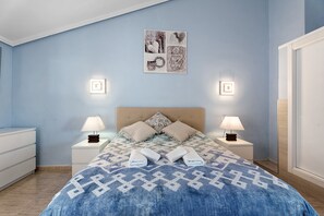 Een slaapkamer met een bed, twee nachtkastjes met lampen, een kunstwerk aan de muur en een kledingkast.