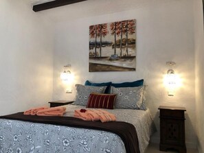 A bedroom with a bed, two nightstands, a painting, and wall sconces.