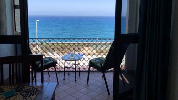 A balcony with two chairs and a small table, overlooking a beach and the ocean. - Holiday Home 'Panoramic Ocean View' with Shared Pool, Wi-Fi and Air Conditioning (Playa del Inglés)