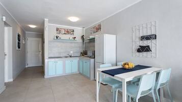 Een kleine keuken met lichtblauwe kastjes, een witte koelkast en een eethoek met een tafel en stoelen.