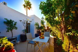 A patio with a table, chairs, potted plants, and a white wall.