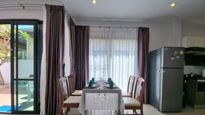 Un comedor con una mesa preparada para cuatro personas, rodeado de sillas, un refrigerador y una zona de cocina.