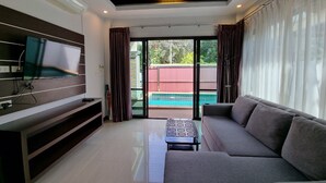 Una sala de estar moderna con una televisión de pantalla plana, un sofá, una mesa de centro y un ventanal corredero que da a una piscina.