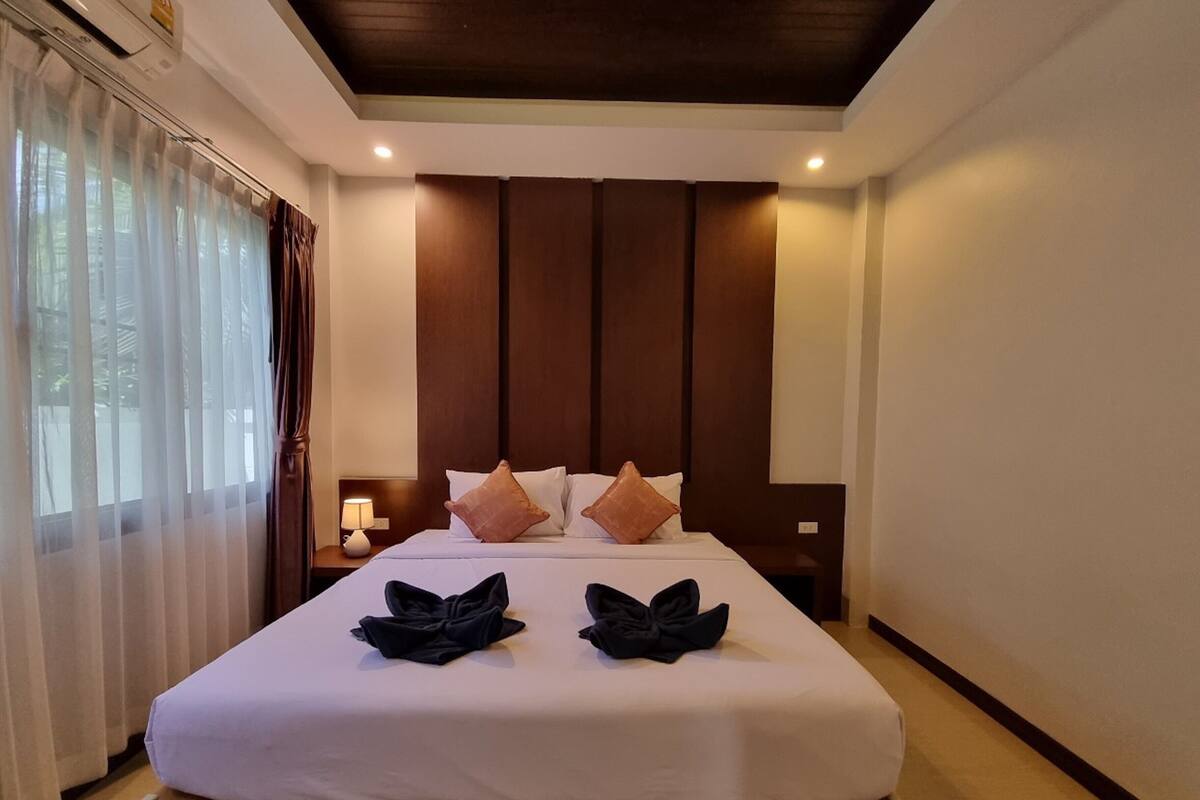 Quarto de hotel com uma cama grande, uma mesa de cabeceira com abajur e uma janela com cortinas.