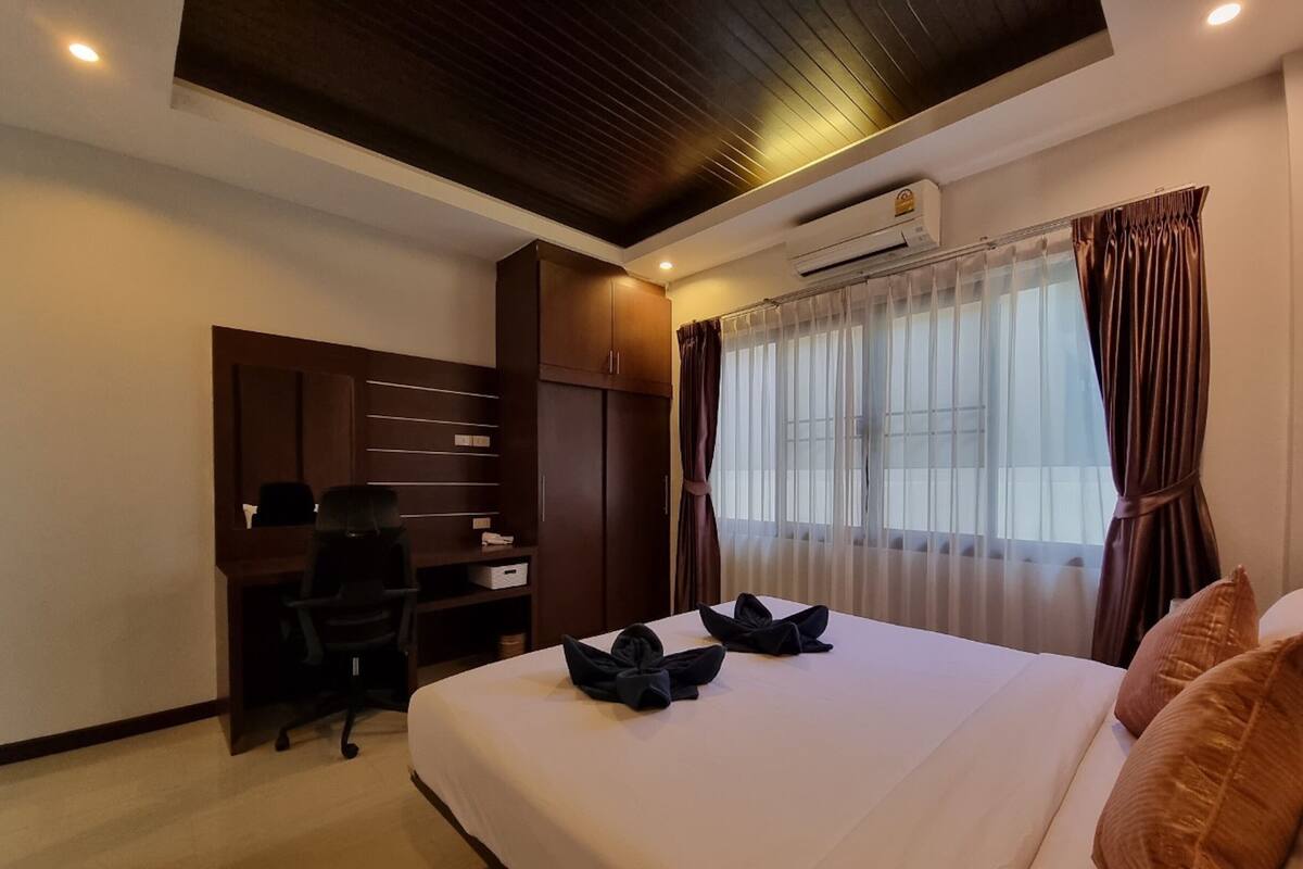 Quarto de hotel com uma cama grande, uma escrivaninha com cadeira, um guarda-roupa e um ar condicionado.