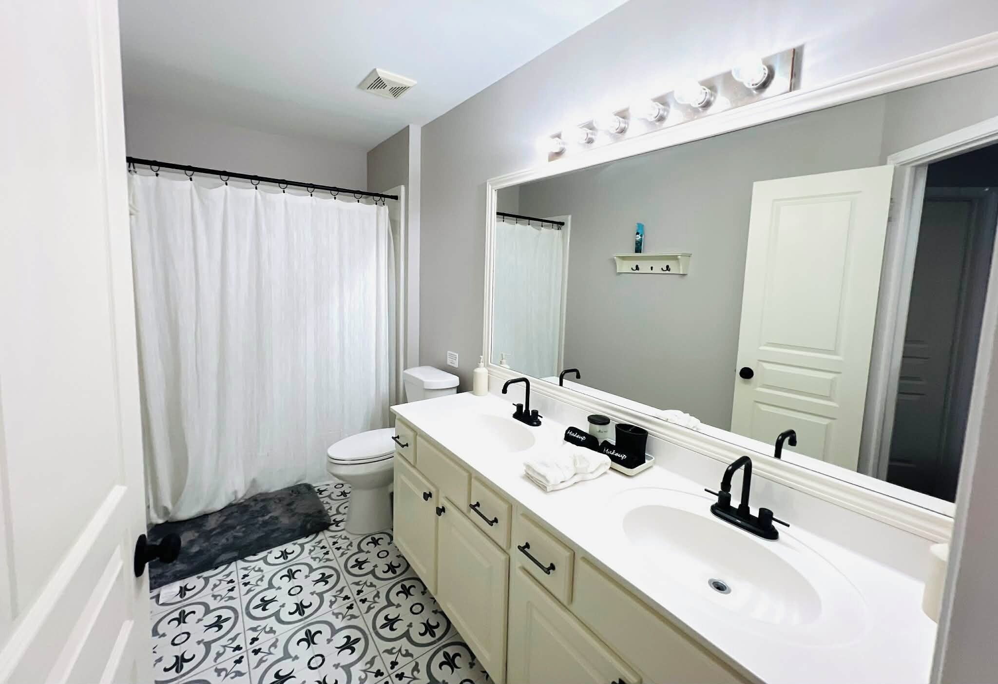 A bathroom with a white sink, two black faucets, a large mirror, and a toilet.