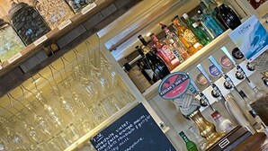A bar area with shelves of various bottles and jars, a selection of glasses, and a chalkboard menu listing drinks. - Clydfan No 1 Trearddur Road (Trearddur Bay)