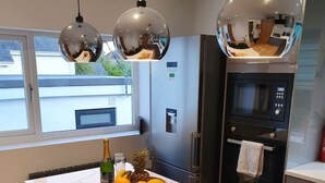 A modern kitchen with a central island, stainless steel appliances, and pendant lighting. - Clydfan No 1 Trearddur Road (Trearddur Bay)