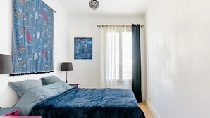 Un dormitorio con una cama, una mesita de noche, una lámpara, una ventana con cortinas y un cuadro en la pared.