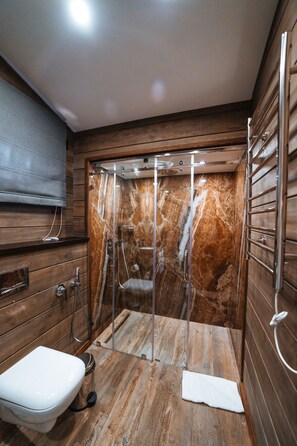 Un baño con tocador de madera, inodoro, ducha con puerta de cristal y pared de mármol.