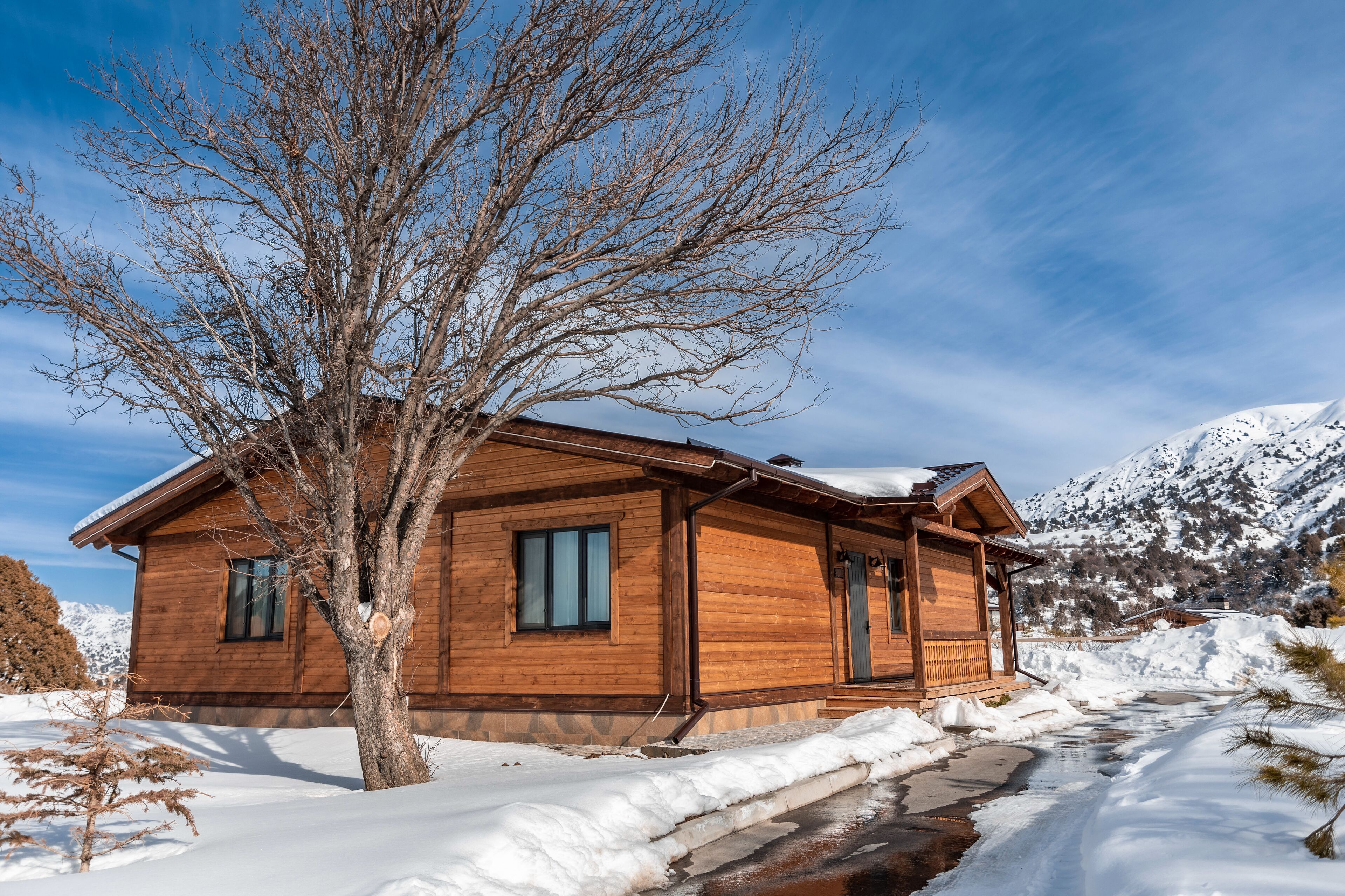A wooden cabin with a snow-covered roof, a wooden porch, and a small stream running in front.
