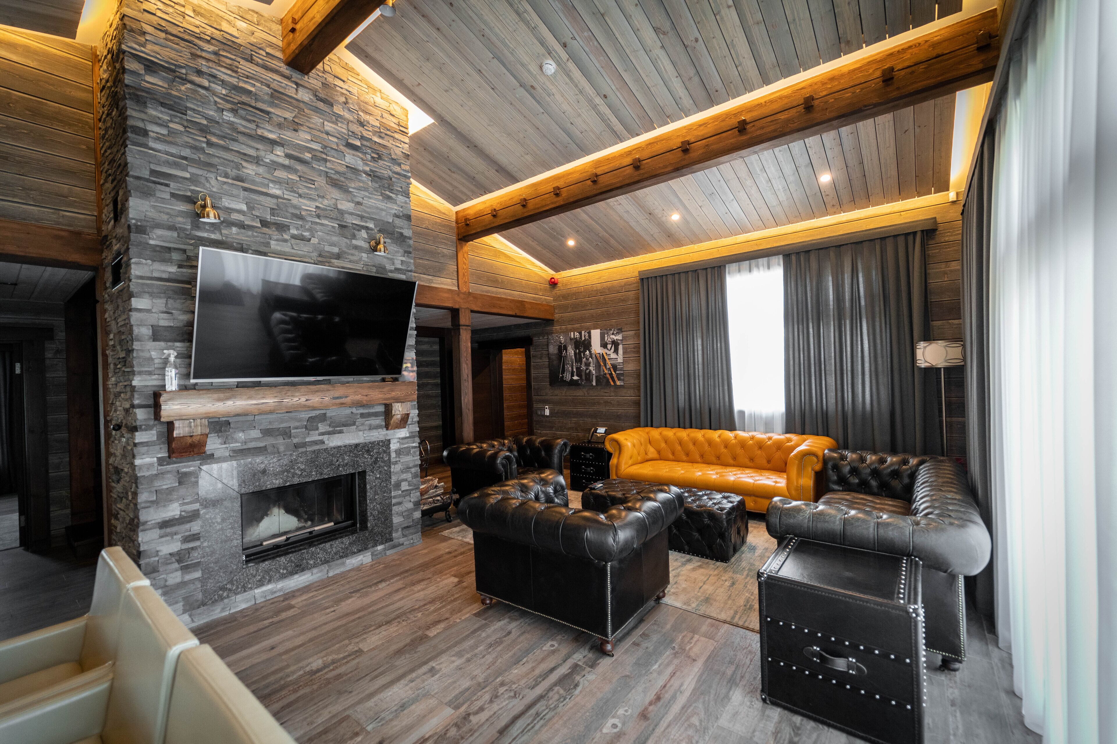 Una sala de estar moderna con chimenea de piedra, sofás de cuero y un televisor de pantalla plana montado en la pared.