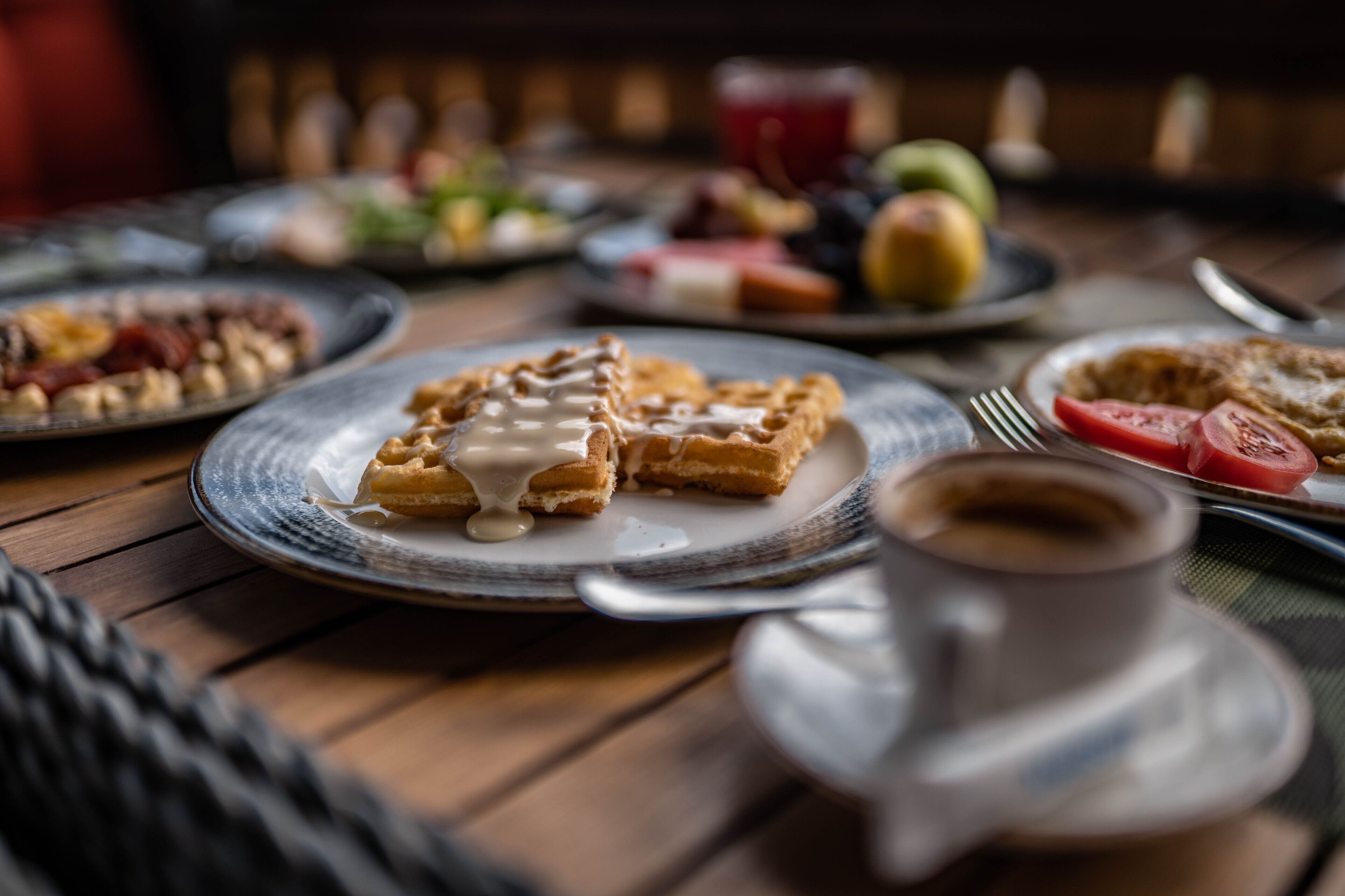 Un desayuno con waffles, café y varias frutas en platos.