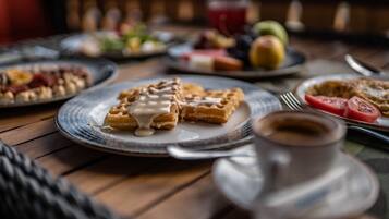 Un desayuno con waffles, café y varias frutas en platos.
