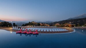 Une piscine d’hôtel avec des chaises longues et des bouées en forme de flamants roses, entourée de bâtiments et de montagnes.