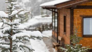 A wooden cabin with a snow-covered roof and a snow-covered tree in the foreground.