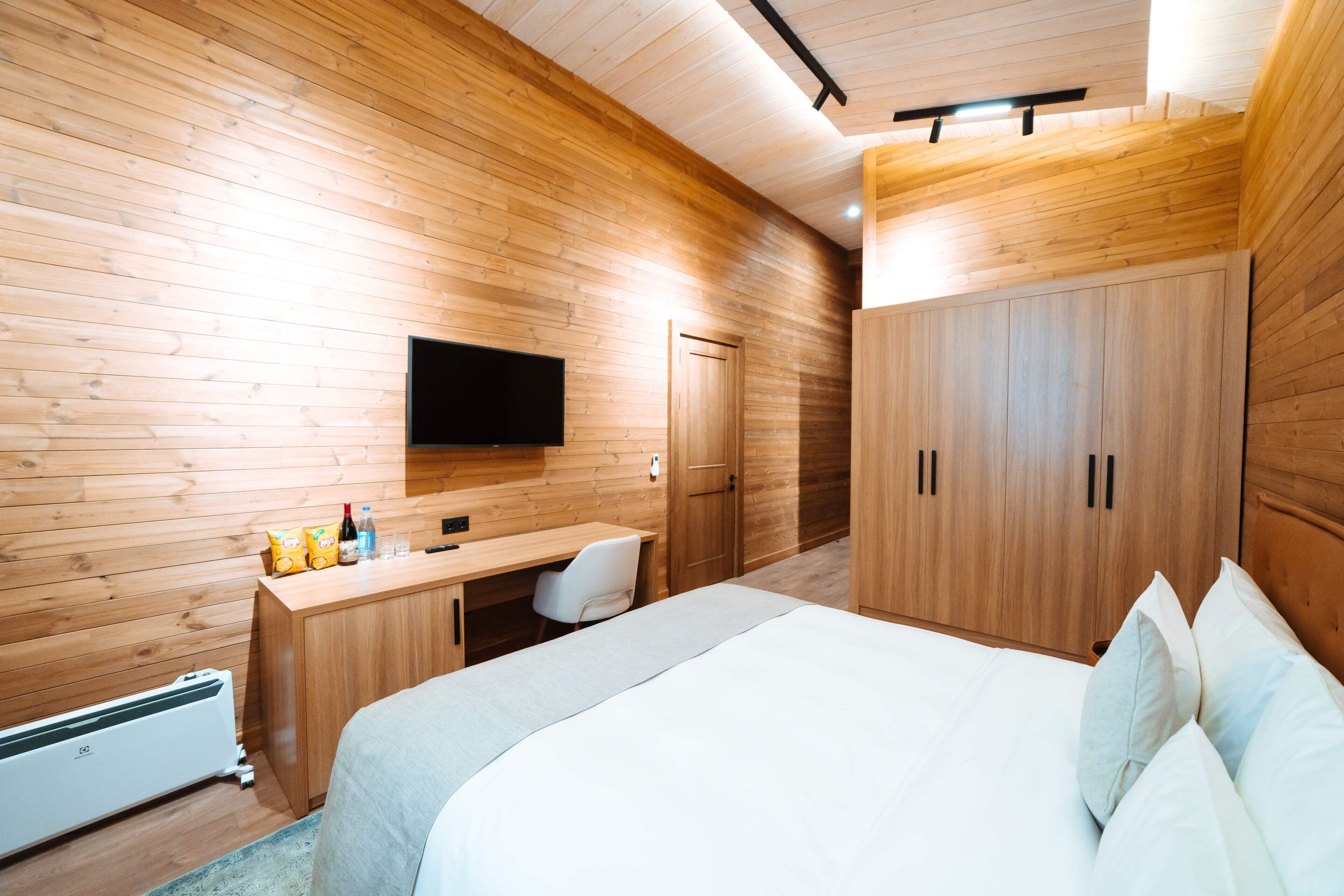 Ein Schlafzimmer mit Holzwänden, einem Bett, einem Schreibtisch, einem Sessel, einem Fernseher und Einbauschränken.