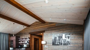 Un vaste espace de vie doté d’un plafond en bois, d’un canapé en cuir, d’un coin cuisine avec des tabourets de bar et d’un tableau accroché au mur.