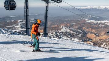 Eine Seilbahn mit Gondeln, eine Person in orangefarbener und grüner Skileidung und eine verschneite Berglandschaft.