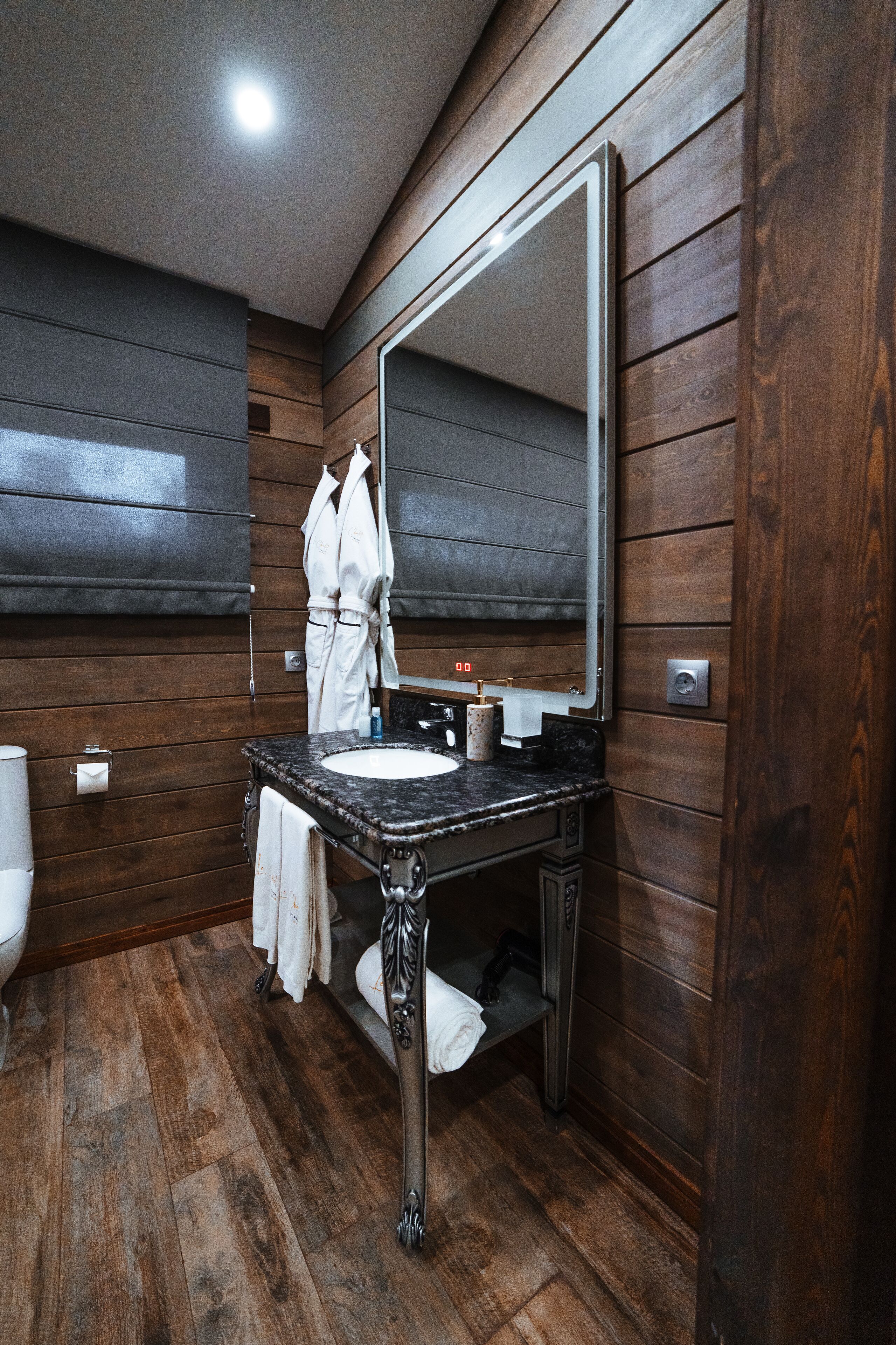 Un baño con paneles de pared de madera, un espejo grande, un lavamanos de mármol y un perchero para toallas.