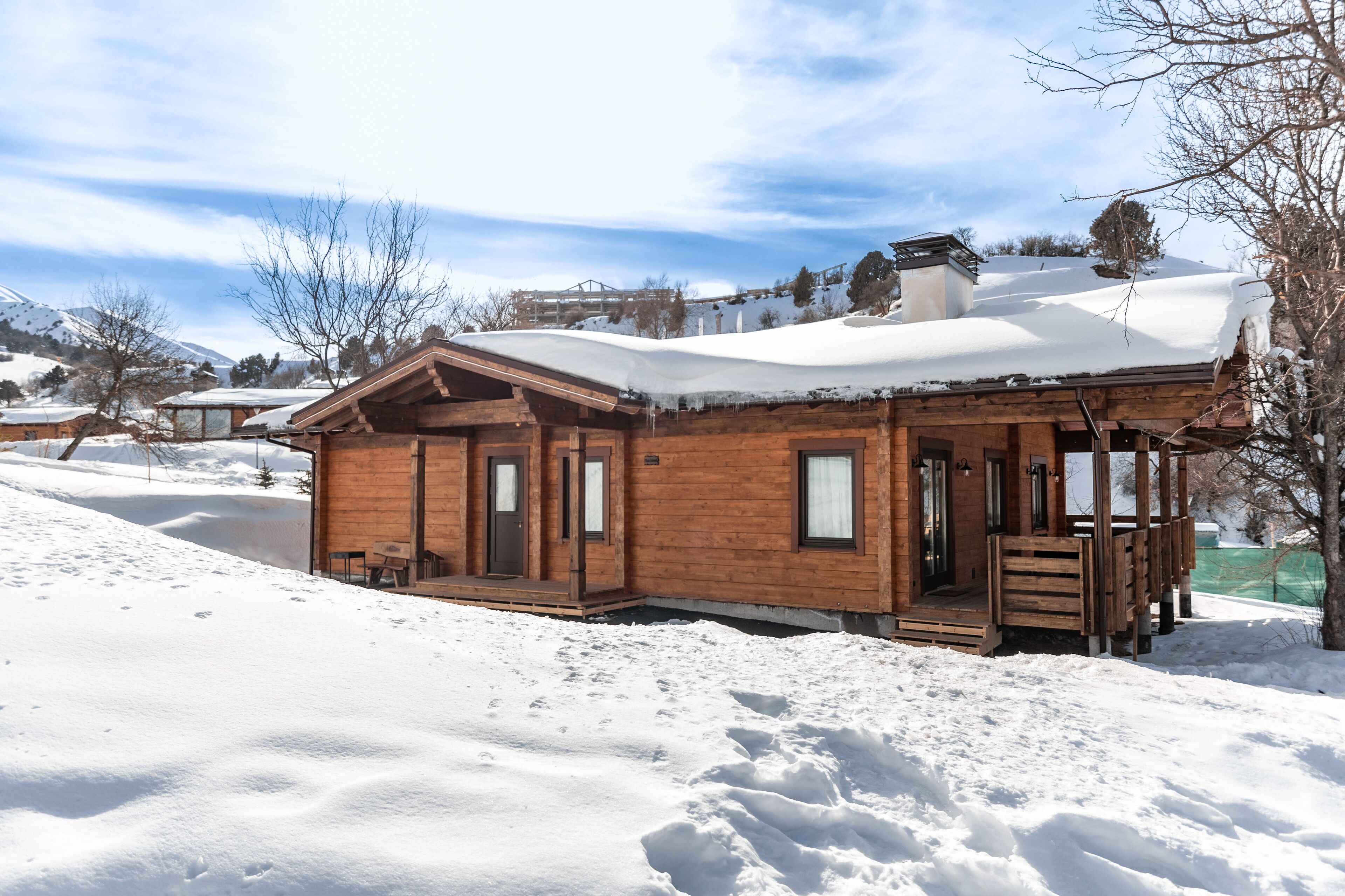 A wooden cabin with a porch, surrounded by snow-covered ground and trees.