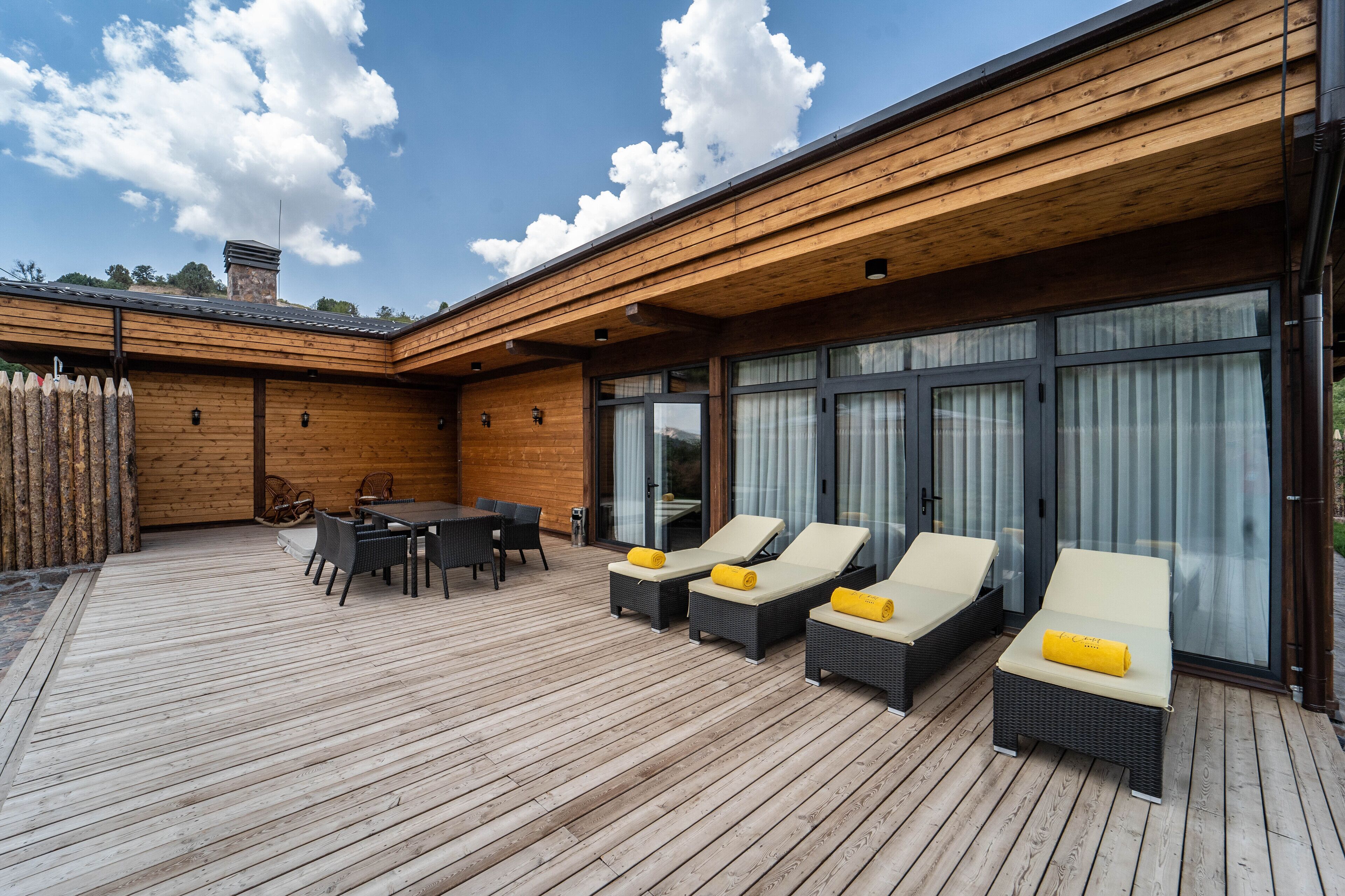 A wooden deck with a table and chairs, and two lounge chairs with cushions.