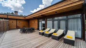 A wooden deck with a table and chairs, and two lounge chairs with cushions.