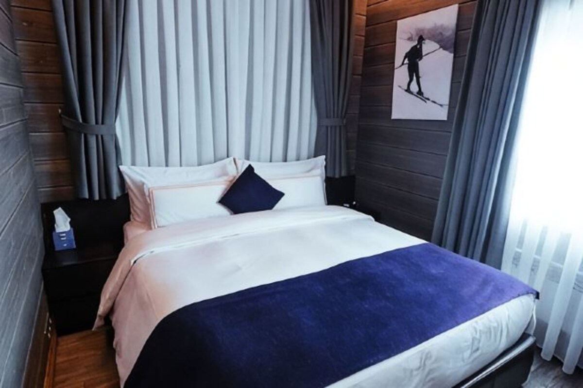 Una cama bien hecha con una manta azul, un almohadón y una mesita de noche con una lámpara.