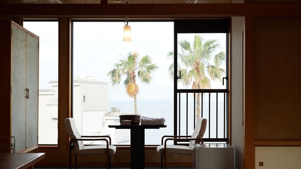 Una habitación con vista a palmeras y al mar, una mesa con sillas y una cama con un futón.