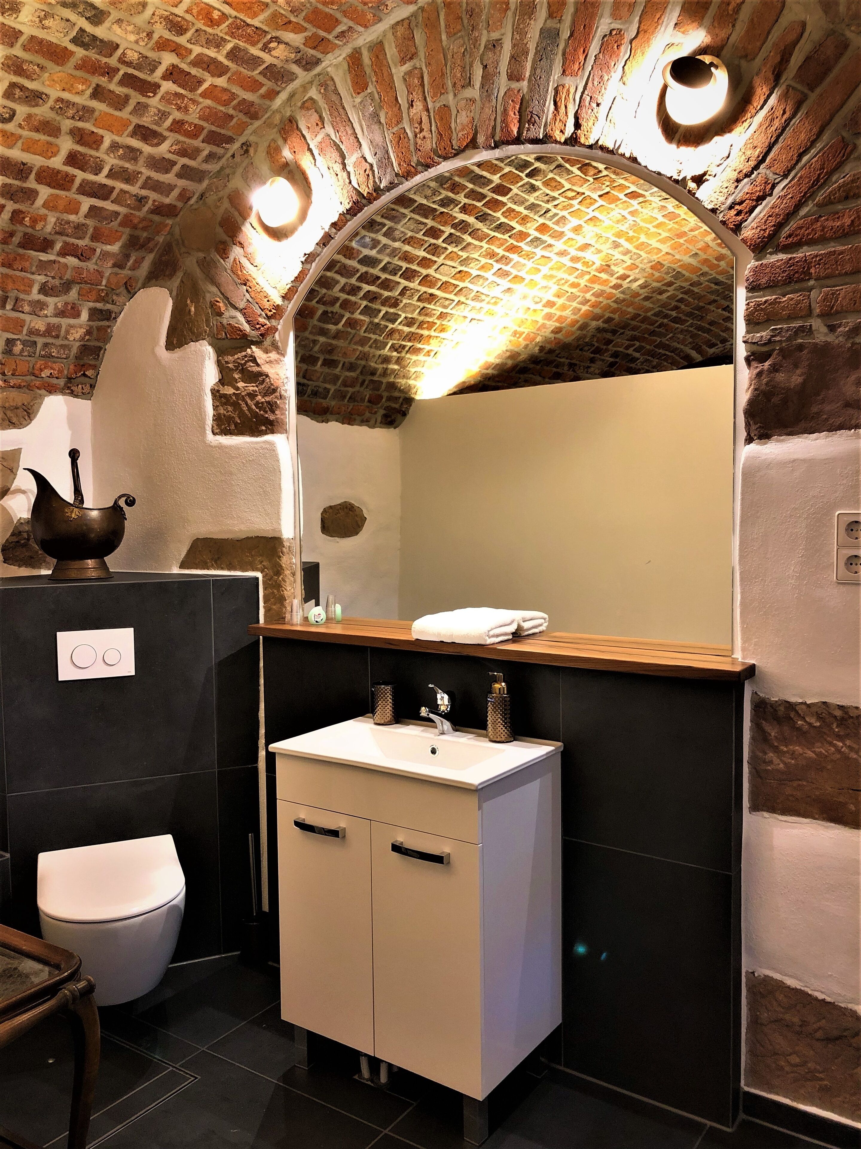 A bathroom with a white sink, dark tiles, a white toilet, and a brick archway.